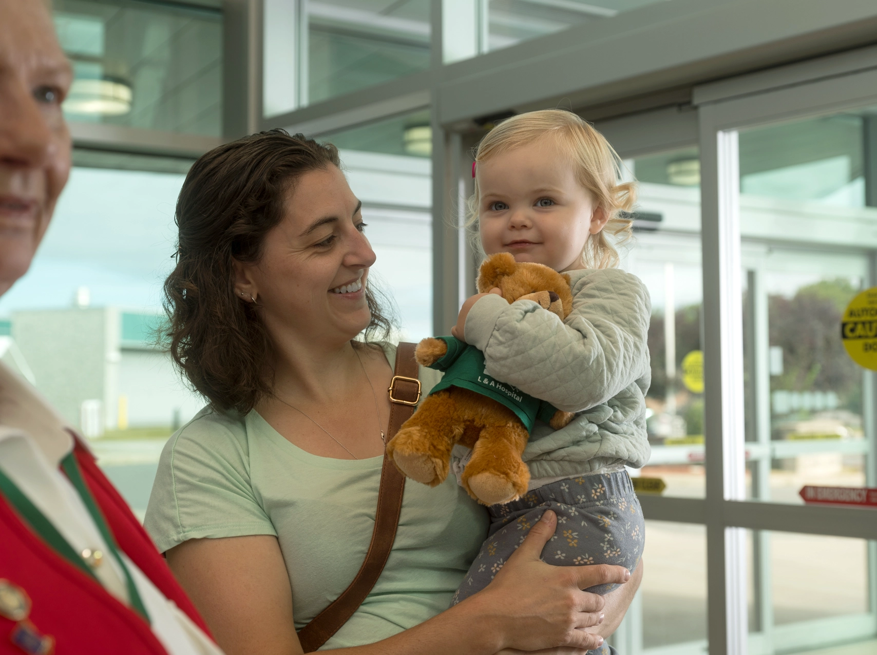 An adult holding a toddler indoors, with the child holding a stuffed toy and looking toward the camera.