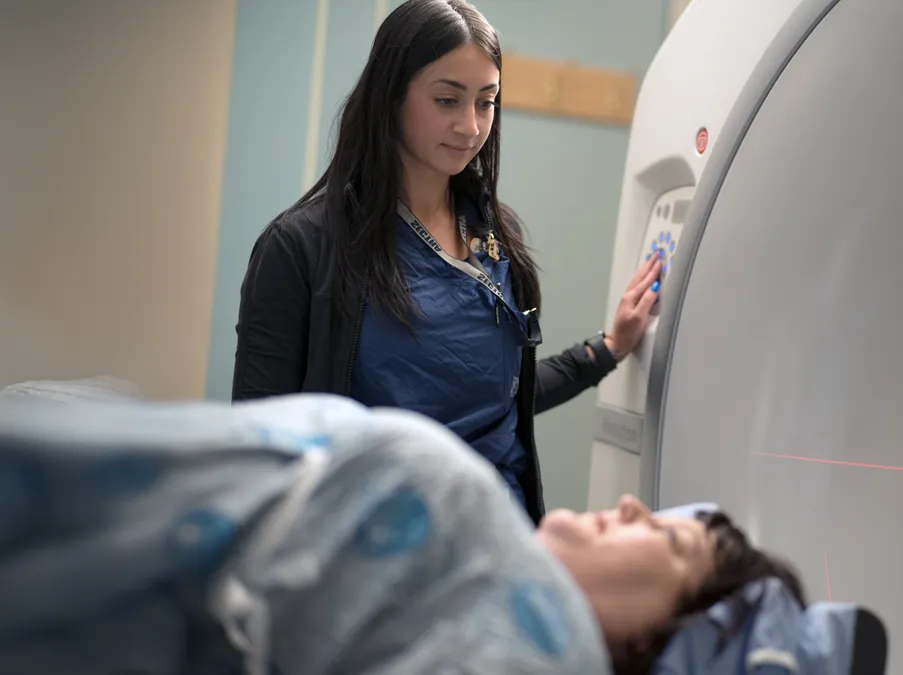 Health-care worker operates a medical imaging scanner while a patient lies on the examination table.