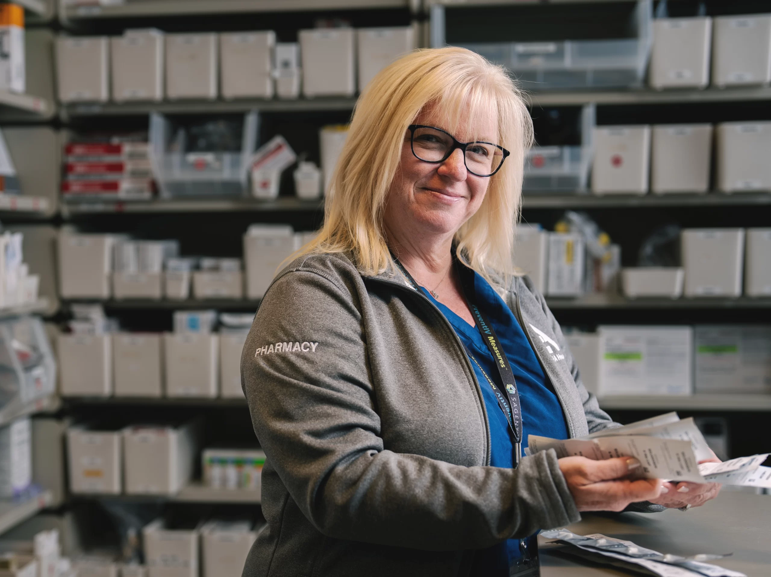 Pharmacy staff member holding packaged medications in a dispensary area.