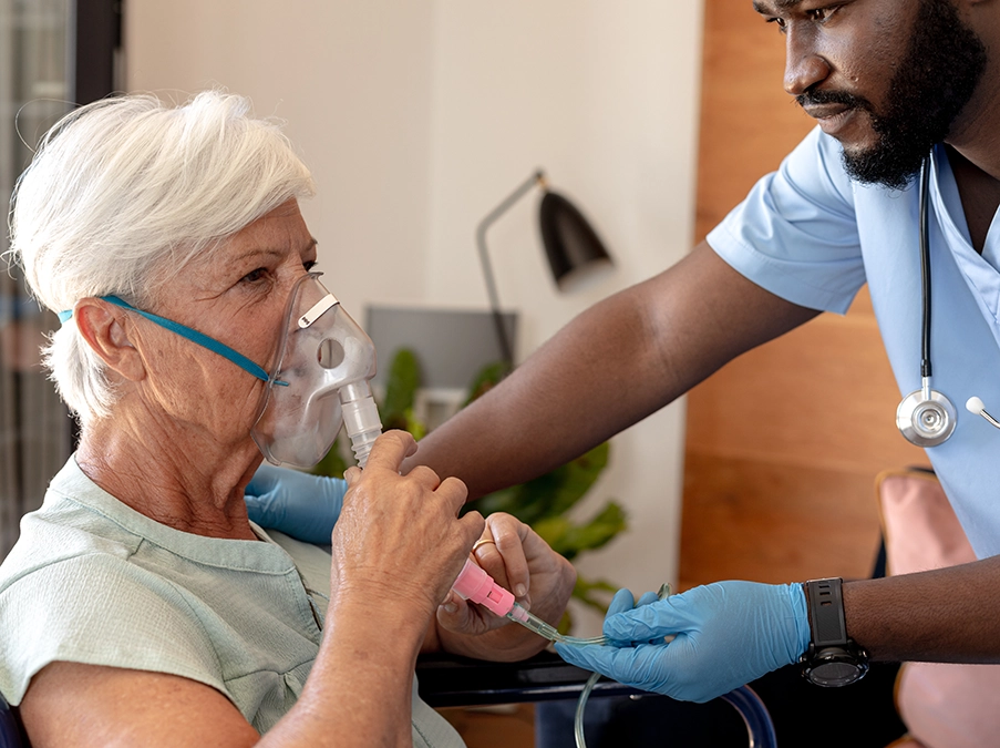 Nurse assisting an older woman using an oxygen mask while adjusting medical tubing.