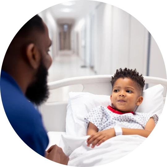Young child lying in a hospital bed while an adult caregiver speaks to them at bedside
