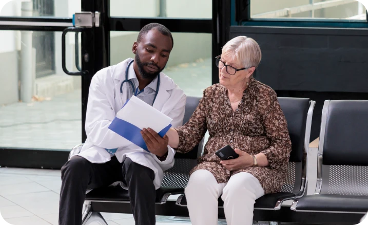 A health-care professional reviewing documents with an older adult seated in a clinic or waiting area.