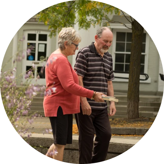 Older adult couple walking together outdoors, one person offering support as they move along a pathway.