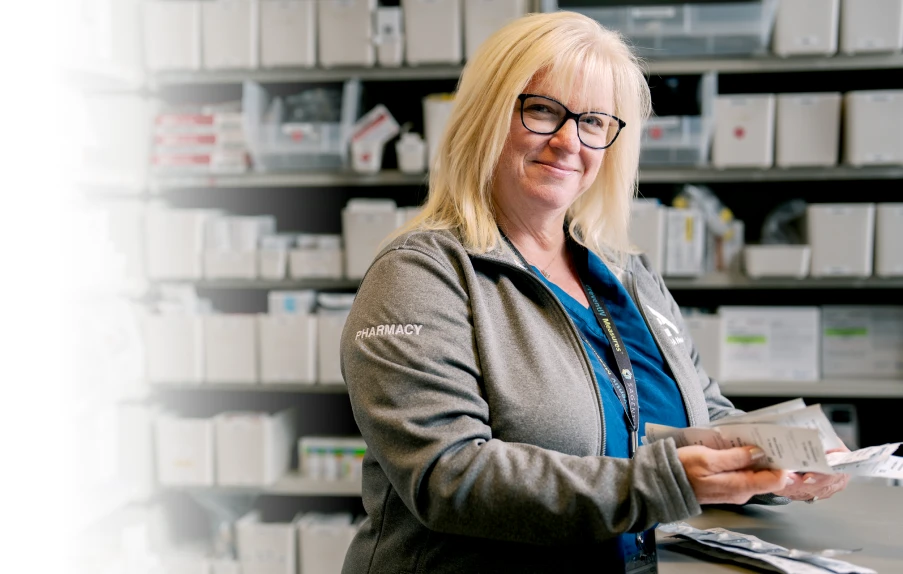 Pharmacy staff member holding packaged medications in a dispensary area.
