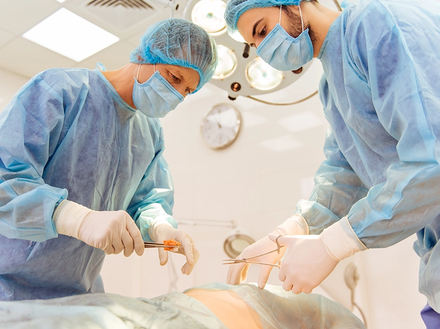 Two surgeons performing an operation in an operating room, wearing masks, gowns, and gloves under surgical lights.