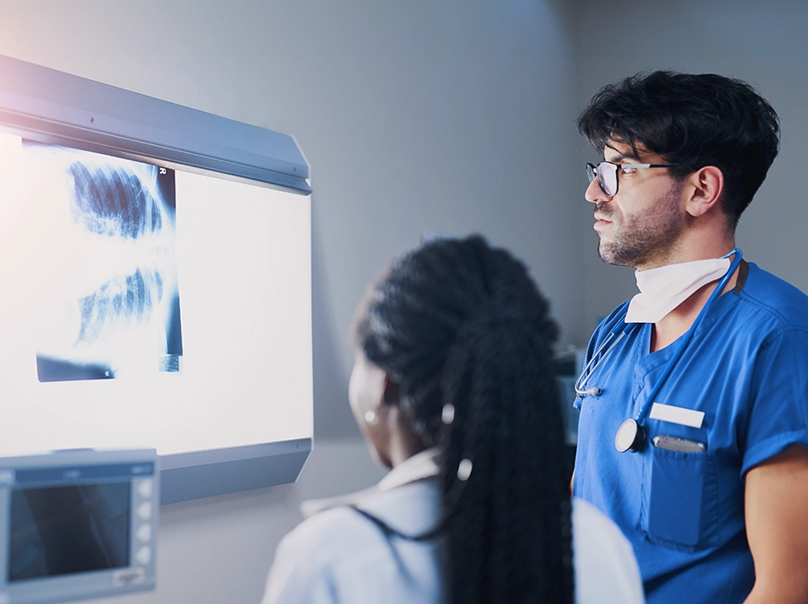 Medical team reviewing an X-ray image on a lighted display in a clinical setting.
