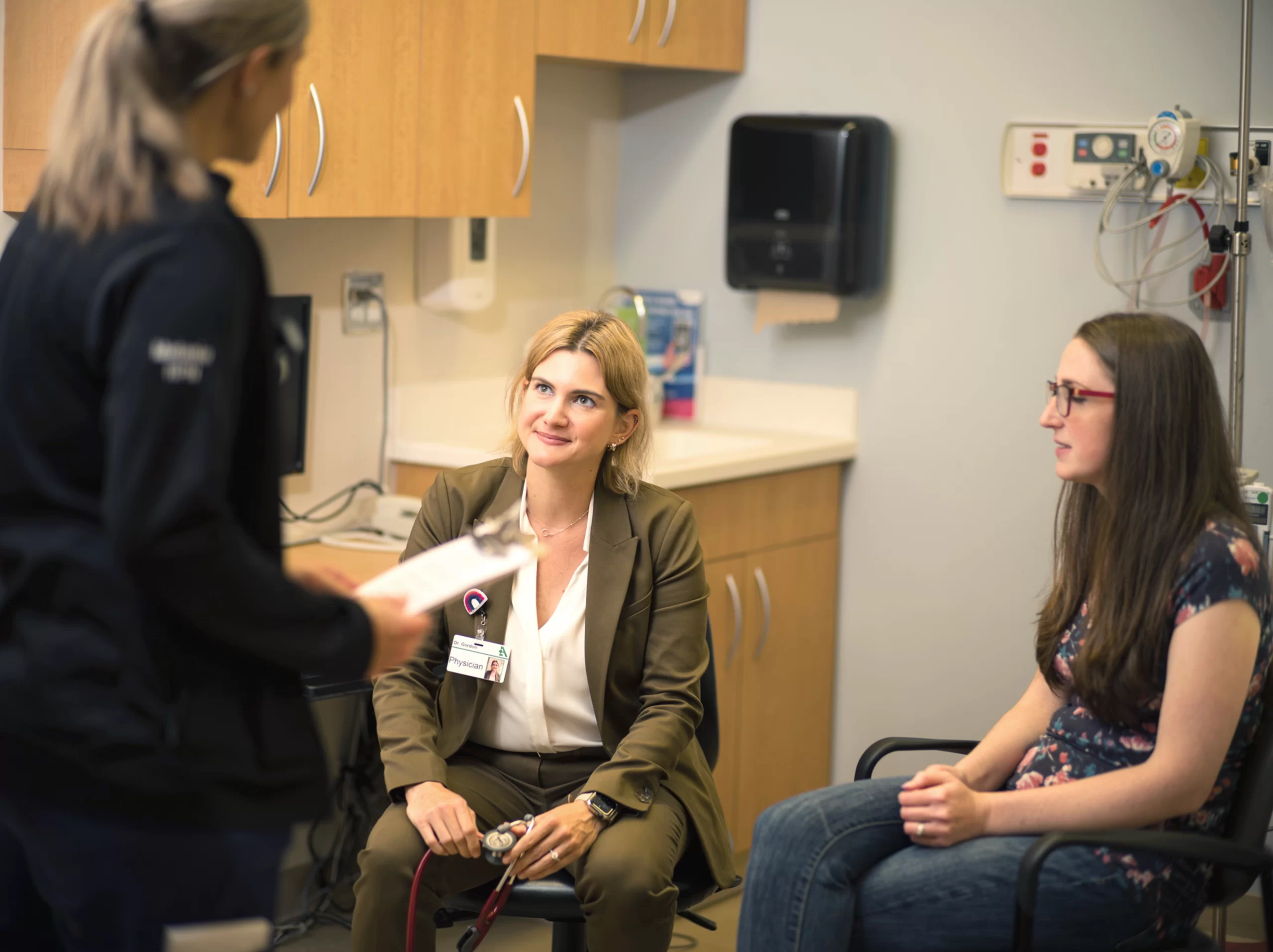 Clinician speaking with two seated women during a medical consultation in an exam room.