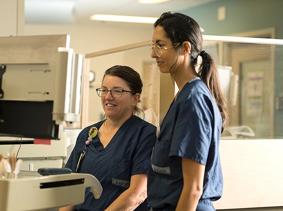 Two clinicians standing beside diagnostic equipment and reviewing information on a screen.