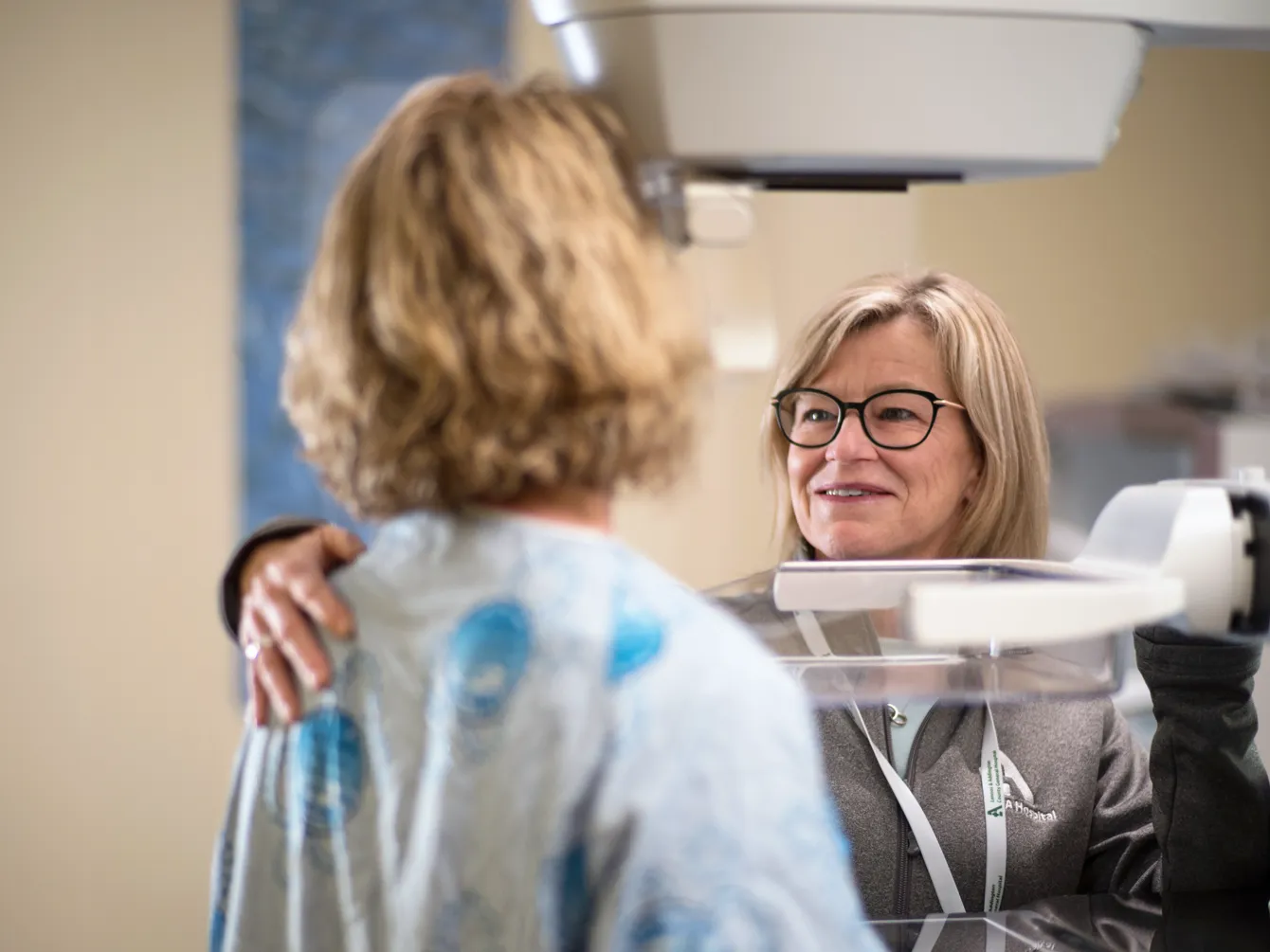 Clinician assisting a patient during a breast imaging exam, offering reassurance during the procedure.